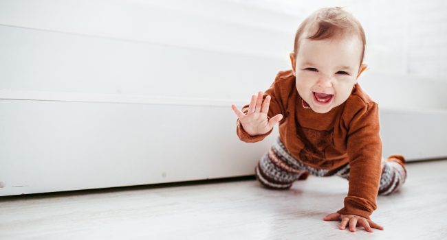 Happy child in orange sweater plays with feather on the floor Happy child in orange sweater plays with feather on the floor